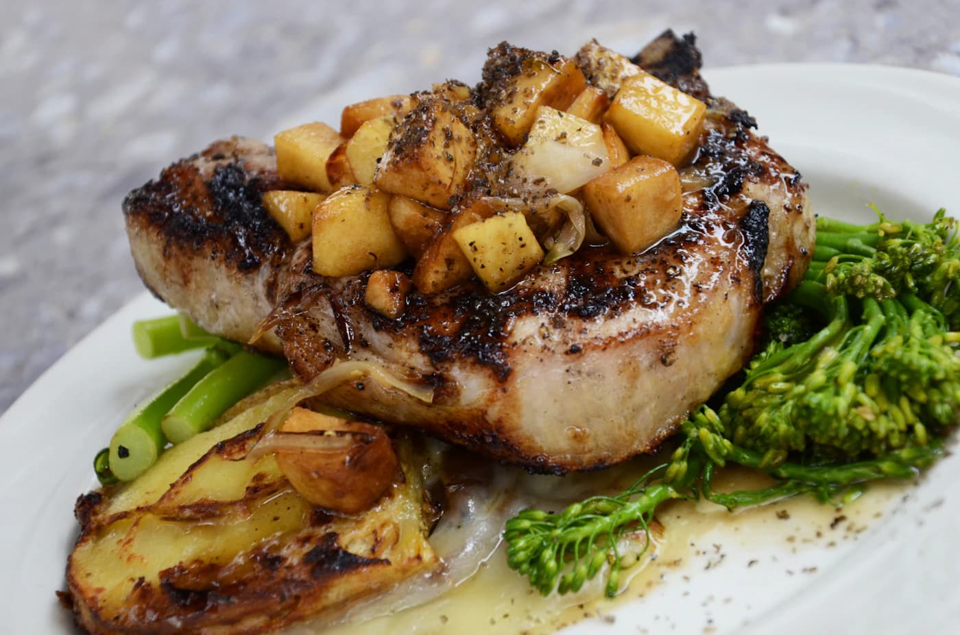 A glazed pork chop topped with caramelised apple and charred greens.