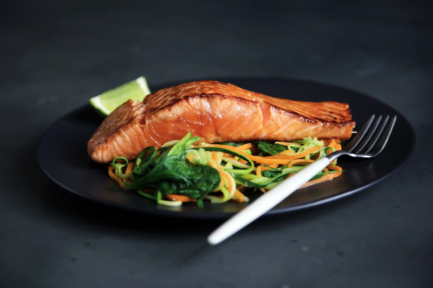 A roasted salmon fillet with ribboned greens on a dark plate.