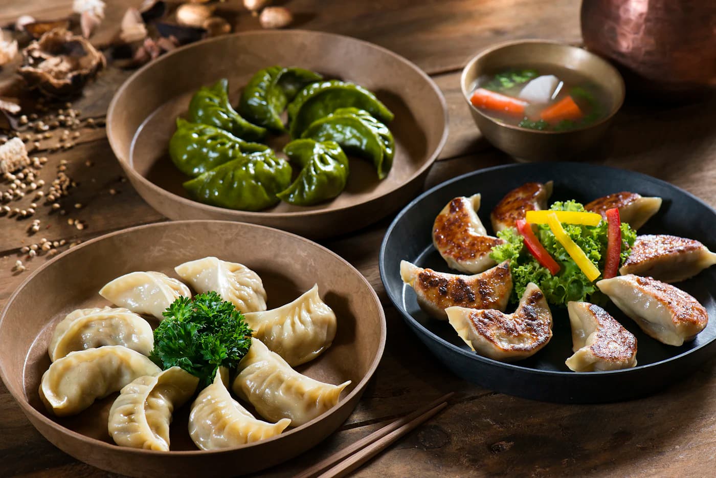 Pleated dumplings in dark bowls with herbs and a dipping sauce.