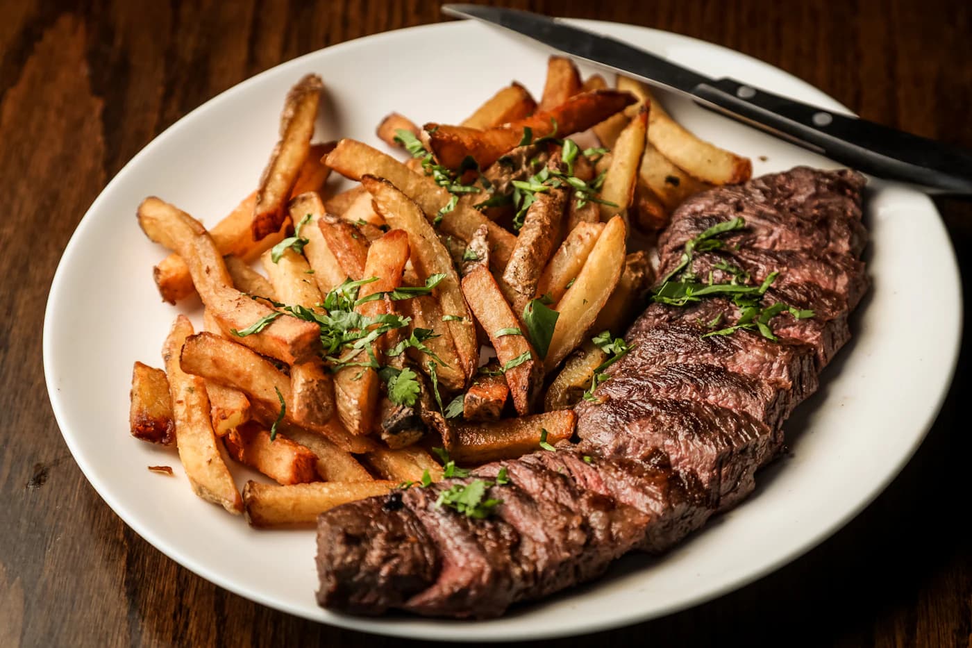 Sliced ribeye steak with seasoned fries on a white plate.